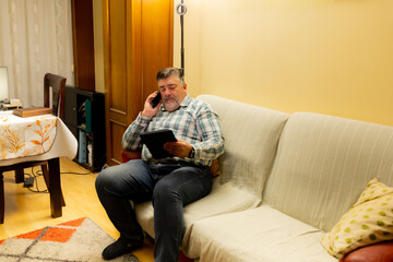 Mature man multitasking using phone and digital tablet