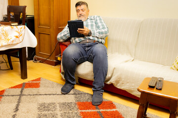 Senior man relaxing on couch using digital tablet