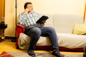 Man multitasking on phone call and tablet on couch