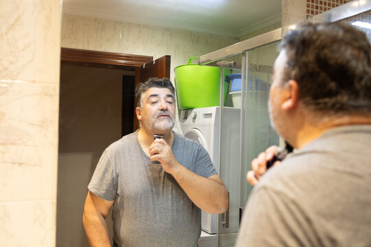 Mature man shaving beard in bathroom mirror