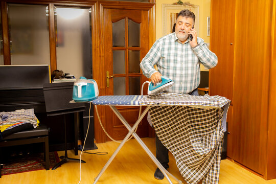 Man multitasking ironing clothes and making a phone call