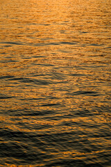 Sea surface view against the sunset light. Background shot of clear golden sea water surface. Gold sea water in calm. Sea texture. 
