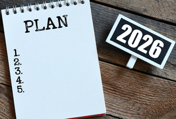 2026 NEW PLAN words in a notebook and a small chalk board on a wooden table. Concept for business.
