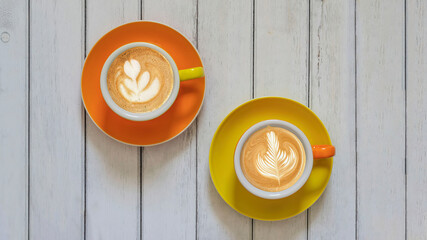 Top view of two colorful cappuccino coffee cups and their saucers on a wooden table.