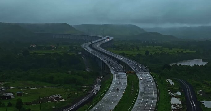 Aerial view of the Mumbai-Nagpur Expressway, also known as Samruddhi Mahamarg, captured during the monsoon season. The modern highway stretches through lush green landscapes, rain-soaked fields.