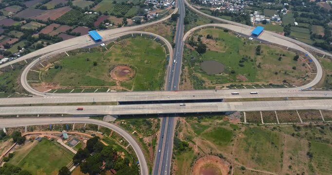 Aerial view of a modern highway interchange in Gujarat, India, showcasing multiple flyovers and well-planned road infrastructure. The cloverleaf junction is surrounded by green fields.