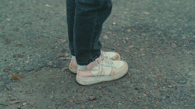 A person stands on a gravel path wearing dirty white sneakers The shoes are scuffed and stained indicating outdoor activities The surroundings are slightly muddy and dull