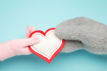 Female hands in warm mittens gives a heart children's hand in gloves on blue background