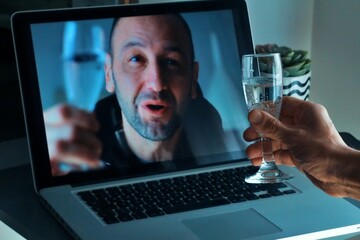 Young man drinking champagne holding sparkler talking to friends on virtual zoom video call celebrate happy new year party in distance online conference chat on computer at home