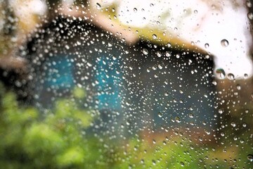 Abstraktes Motiv mit Regentropfenmuster vor Garten mit grauer Hütte aus Holz und blauen Fenstern vor weißem Himmel mit Licht bei Regen und Sturm am Nachmittag im Herbst