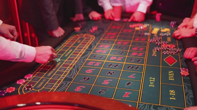 Casino table with roulette wheel in motion, with casino chips, tokens, the hand of croupier, dollar money and a group of gambling rich people playing bet on a party, blue poker table and deck of cards