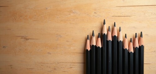 Multiple sharpened black pencils arranged in ascending order on wooden surface. Pencils lined up close together creating visual graph like effect, ready for drawing writing. Represents ideas,