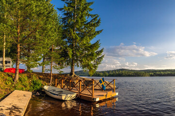 Swedish lake landscape with a dock, rowboat, and flag reflecting evening light