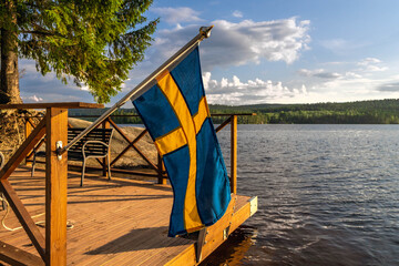 Swedish flag waving over lake reflecting scenic landscape
