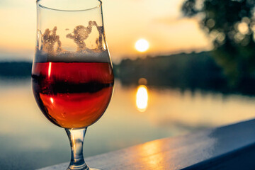 Beer glass reflecting sunset over a calm lake in Sweden