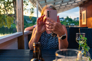 Woman photographing sunset lake view with smartphone in Sweden