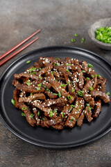 Fried teriyaki beef with sesame seeds and green onions on a brown background. Asian cuisine.