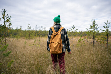 Woman backpacker move across wetland landscape with dense dry sedge grass and cloudy horizon above. Outdoor trail activity, nature exploration, boggy ground wild navigation, female hiking adventure