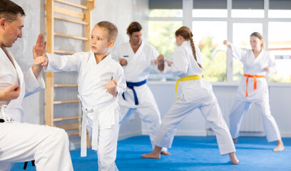 Boy in kimono practices combat technique of punching and blocking with trainer at family martial arts class
