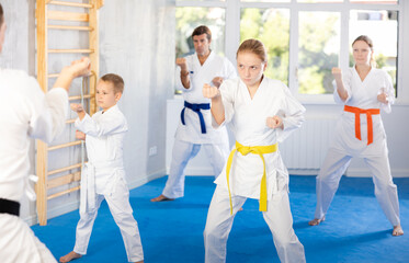 Teen girl and her family repeat movements and learn fighting techniques during martial arts lesson....