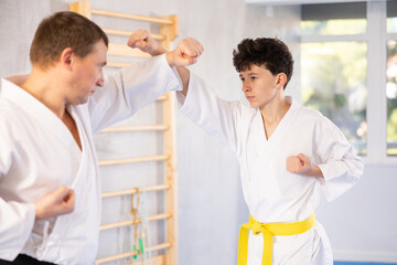 Active teen male karate practitioner training battling methods with middle-aged partner in sports hall