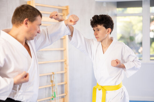 Active teen male karate practitioner training battling methods with middle-aged partner in sports hall