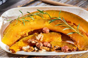 Roasted pumpkin wedges served with toasted hazelnuts and drizzled with honey, creating a warm and...