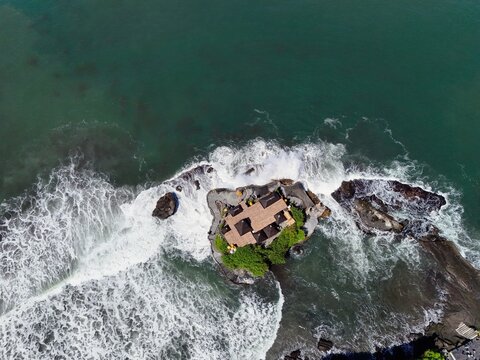 Aerial view of a beautiful coastal Tanah lot temple, Bali , Indonesia surrounded by ocean waves and lush greenery, showcasing dramatic cliffs and scenic tropical landscape.