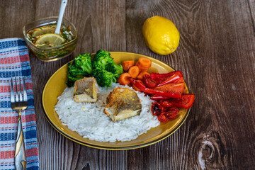 A perfectly roasted fish fillet served on a plate with steamed rice, broccoli florets, and sliced carrots. The golden-brown fish contrasts beautifully with the vibrant green broccoli and bright orange
