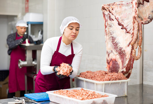 Positive young butcher shop saleswoman standing at cutting table, demonstrating fresh raw mincemeat
