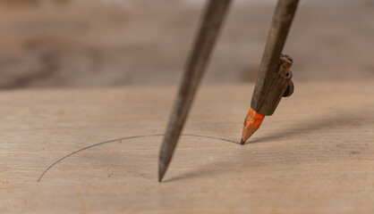 Un compas de menuisier en train de tracer un trait sur une planche de bois.