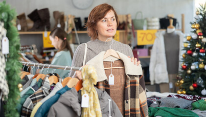 Woman chooses jacket and coat for the winter period in a fashionable clothing store