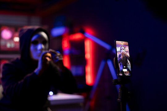 Close up of mobile phone used by hacker concealing identity filming ransom video in hidden apartment. Smartphone on tripod used by rogue programmer with mask to record blackmail footage
