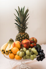 a bowl of fruit display with pineapple, oranges, bananas, grapes, peaches and more