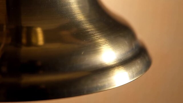 Close-up of the polished lower edge and skirt of a large shiny golden brass bell indoors