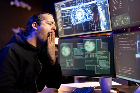 Tired hacker at desk yawning after coding all night, using AI to evade security with stealth malware. Exhausted man feeling sleepy while trying to hide malicious code from firewall detection systems