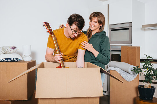 Couple Unpacks From Cardboard Box Guitar Together In New Apartment