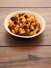A bowl of dried fruit with yellow and red raisins, cranberries. The bowl is on a wooden table. Natural high sugar and glucose content. Popular snack.