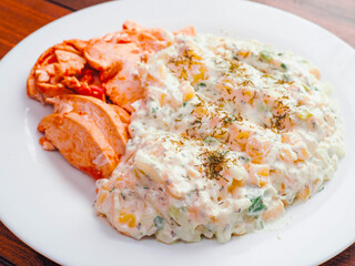 Portion of potato and corn salad and red hot slices of Cajun chicken fillet on a white plate. Simple tasty dinner.