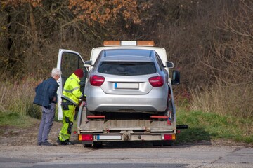 Fototapeta premium elderly man watches as his car is secured to a tow truck