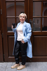 A blonde woman in a white sweater and scarf stands outside a business building. The architecture of the building is dominated by red brick.