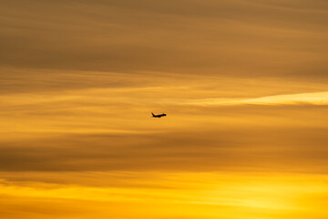 Passenger airplane silhouette in flight against a dramatic golden and orange sky during a beautiful sunset.