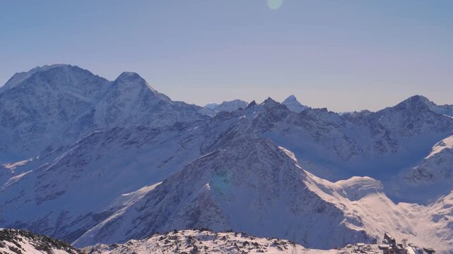 panoramic view of the snow covered peaks of the Greater Caucasus mountain range in Russia on a clear, sunny winter day. The footage captures the vast, pristine landscape, highlighting the majestic sca