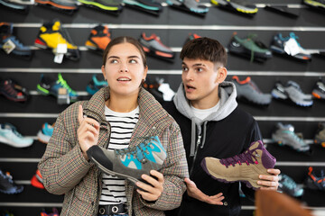 Smiling young couple in sports shop to choose trekking winter shoes