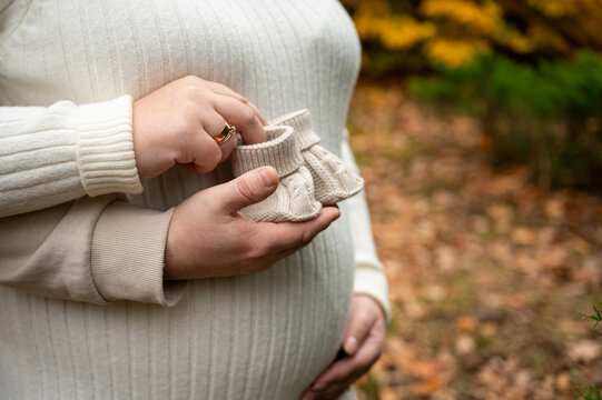 Close-up of an expectant couple's hands: the mother embraces her pregnant belly, while the father gently holds a pair of tiny knitted baby booties - Powered by Adobe