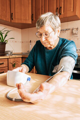 An elderly woman measures her blood pressure in the kitchen. Health maintenance, healthy aging, disease prevention, cardiovascular system monitoring, home treatment