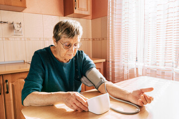 An elderly woman measures her blood pressure in the kitchen. Health maintenance, healthy aging, disease prevention, cardiovascular system monitoring, home treatment