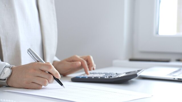 Businesswoman is calculating annual tax using calculator and taking notes in the office, managing domestic budget and checking financial documents. Audit and taxes in business
