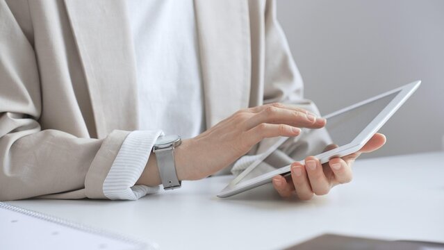 Professional woman working on tablet at desk, checking digital content with notebook and glasses nearby, focused on online tasks. Business people concept