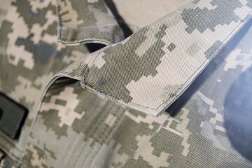 Close-up of a durable, camouflage military uniform piece with green and brown shades, detailed stitching, and a nearby light source